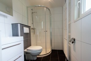 Uma casa de banho moderna com cabine de duche em vidro, sanita e lavatório branco.