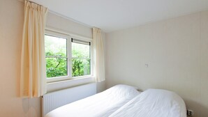 A bedroom with a single bed, a window with curtains, and a radiator. - Chalet Near Campground (De Bult)