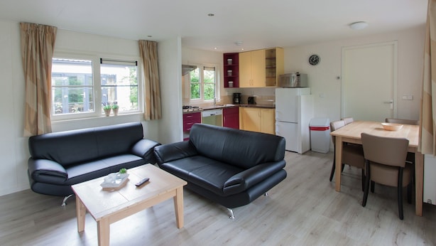 A compact living space with a sofa, a small table, a kitchenette, and a dining area. - Chalet Near Campground (De Bult)