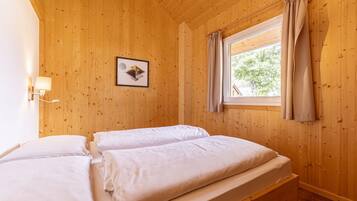 A wooden-paneled room with two beds, a window with curtains, and a wall-mounted lamp.