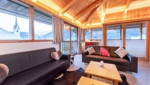 A cozy room with a wooden ceiling, a black sofa, a wooden coffee table, and a view of a mountain. - Spacious Stay With Mountain View (Wald im Pinzgau)