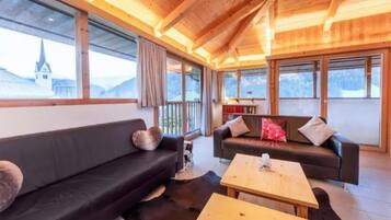 Une pièce chaleureuse avec un plafond en bois, un canapé noir, une table basse en bois et une vue sur une montagne.