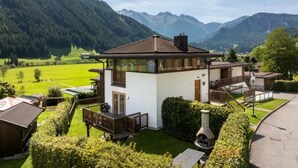 A two-story chalet with a balcony, surrounded by a well-maintained garden and a view of mountains. - Spacious Stay With Mountain View (Wald im Pinzgau)