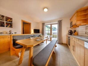 A modern kitchen with wooden cabinets, a dining table with benches, and a television. - Spacious Stay With Mountain View (Wald im Pinzgau)