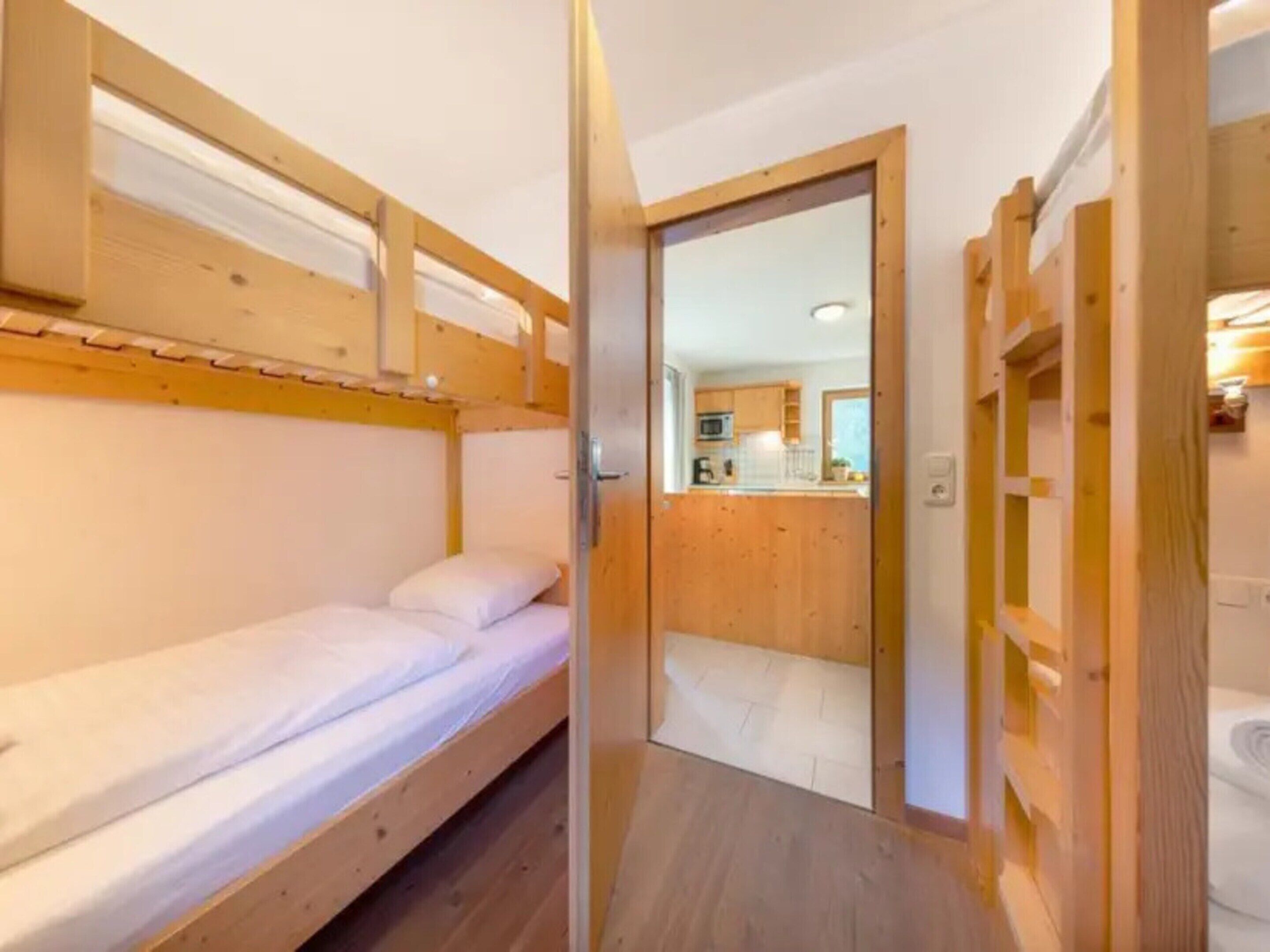 A bunk bed room with a wooden door leading to a kitchen area.