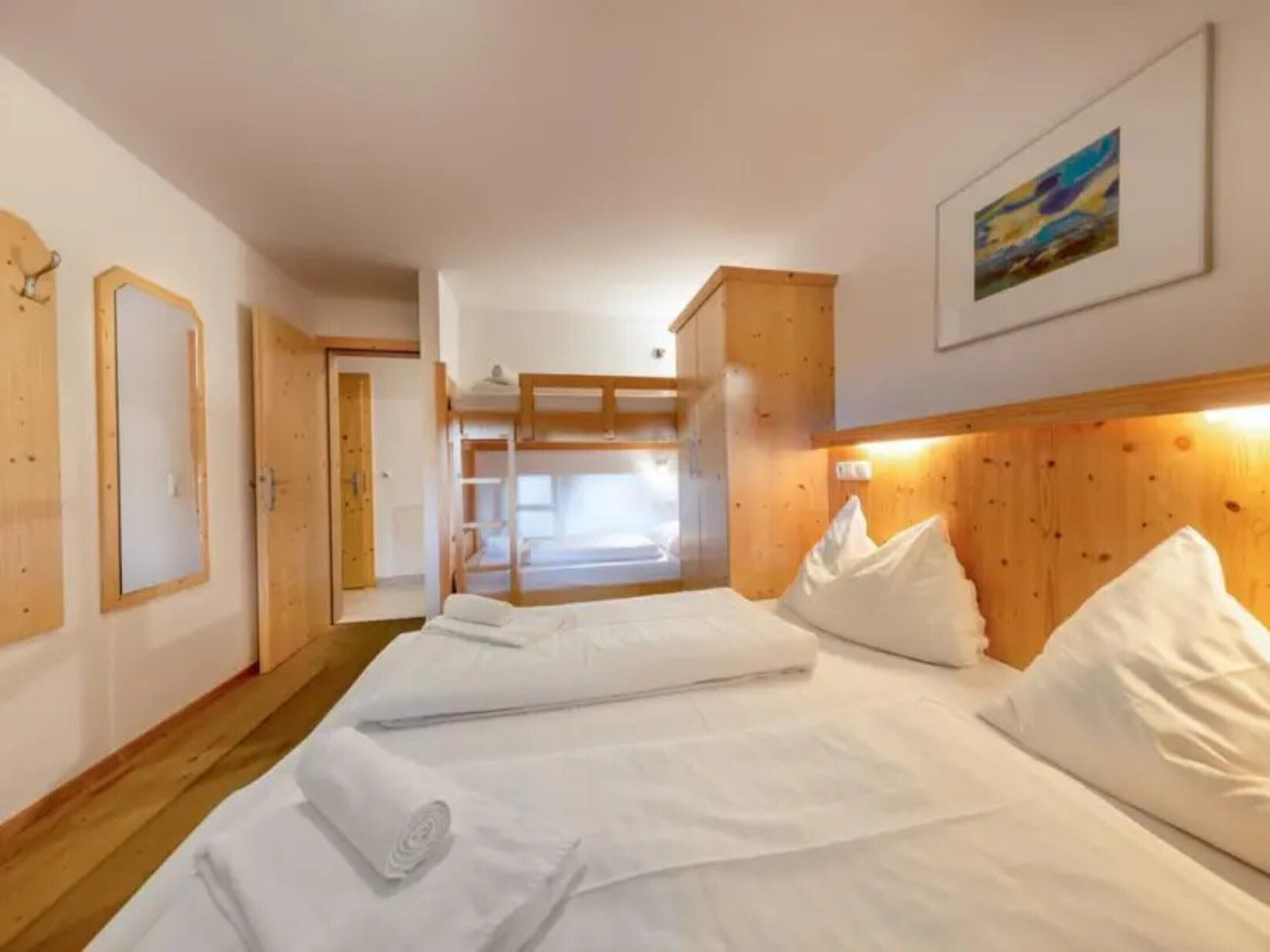 Une chambre d’hôtel avec des lits superposés, des murs en bois, un tableau encadré et une porte donnant sur une autre pièce.