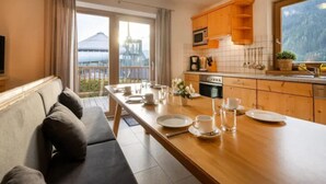 A modern kitchen with wooden cabinets, a dining table set for four, and a view of a mountain through the window. - Spacious Stay With Mountain View (Wald im Pinzgau)
