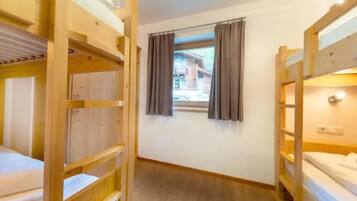 Une chambre avec des lits superposés, une fenêtre avec des rideaux et une vue sur un bâtiment à l’extérieur.