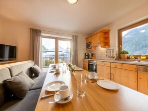 A modern kitchen with wooden cabinets, a dining area with a table set for two, and a television on the left. - Spacious Stay With Mountain View (Wald im Pinzgau)