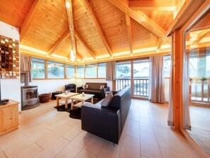 A cozy cabin interior with a fireplace, a sofa, a dining table, and large windows. - Spacious Stay With Mountain View (Wald im Pinzgau)