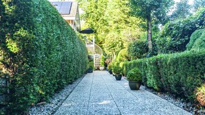 A pathway lined with neatly trimmed hedges and potted plants, leading towards a building with a staircase. - Apartment in Oostkapelle Near the Beach (Oostkapelle)