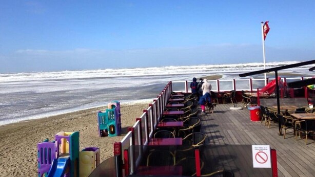 A beachside restaurant with outdoor seating, a view of the ocean, and a flag indicating no swimming. - Apartment in Oostkapelle Near the Beach (Oostkapelle)
