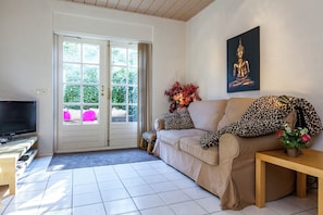 A living room with a beige sofa, a television, a Buddha painting, and a door leading to a balcony. - Apartment in Oostkapelle Near the Beach (Oostkapelle)