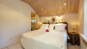 A bedroom with a wooden ceiling, a large bed with white bedding, two bedside lamps, and a small table with a lamp. - Apartment in Oostkapelle Near the Beach (Oostkapelle)