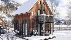 A wooden cabin with a balcony and a covered outdoor seating area, surrounded by snow and mountains. - Holiday Home on the Kresichberg With Swimming Pool (Sankt Georgen am Kreischberg)