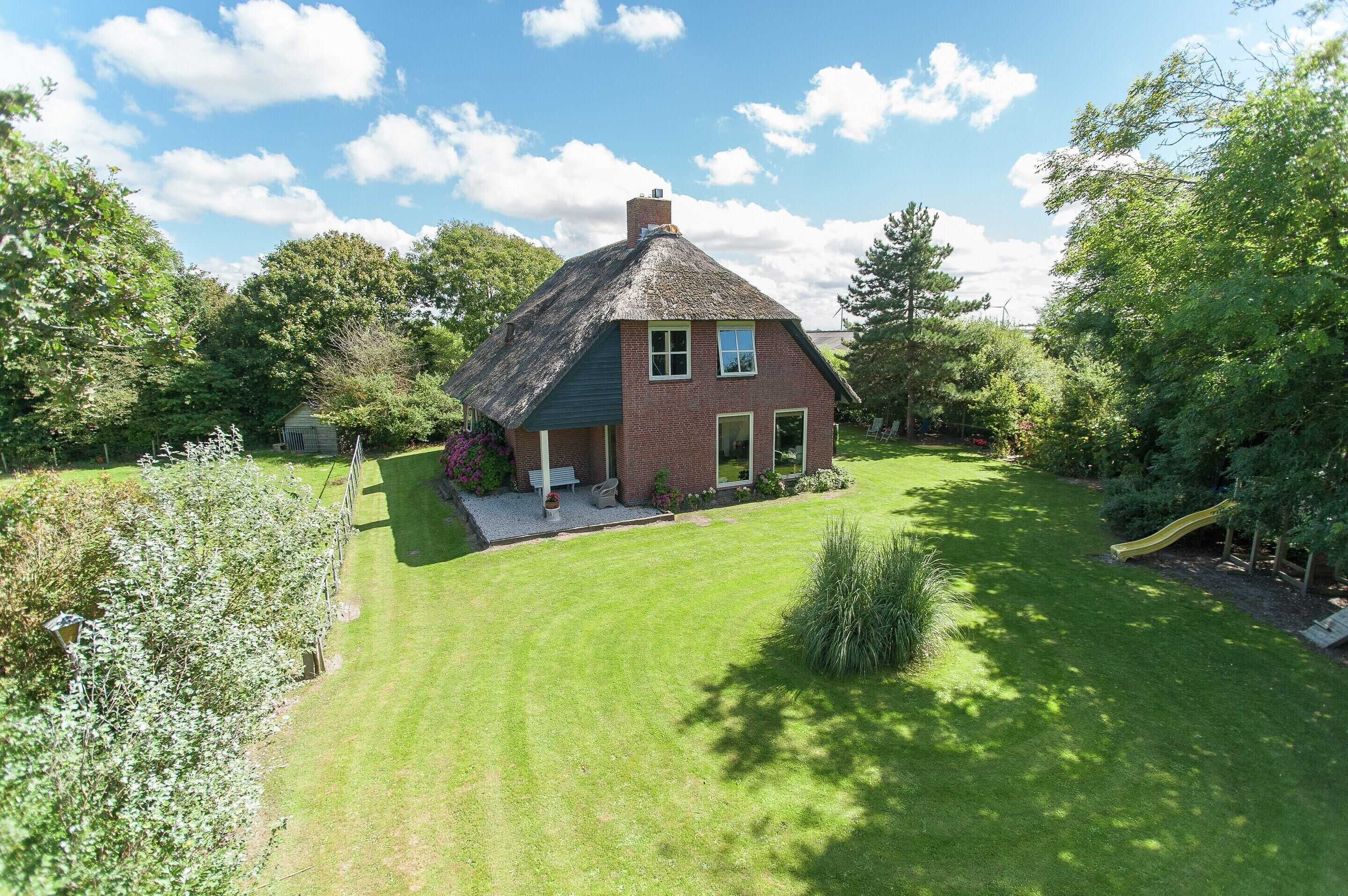 A house with a thatched roof, surrounded by a well-maintained lawn and trees.