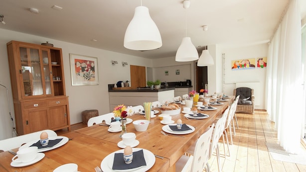 A dining area with a long wooden table set for breakfast, white chairs, and pendant lights. - Luxurious Mansion in Callantsoog With Sauna (Callantsoog)