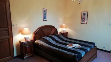 A bedroom with a bed, two bedside tables with lamps, a chandelier, and two framed pictures on the wall.