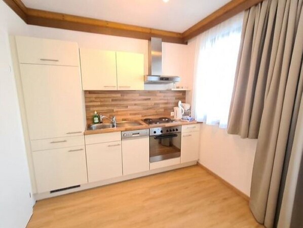 Une cuisine de taille réduite avec des meubles blancs, un plan de travail en bois, une cuisinière et une fenêtre agrémentée de rideaux.