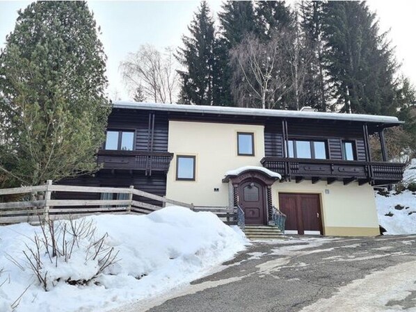 A two-story building with a wooden balcony, a front door, and a snow-covered driveway. - Cushy Apartment in Bad Kleinkirchheim near Ski Area (Bad Kleinkirchheim)
