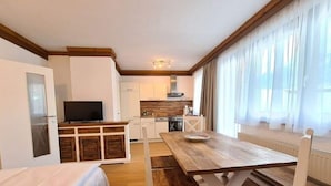 Een gezellige kamer met een bed, een houten tafel en een kitchenette op de achtergrond.