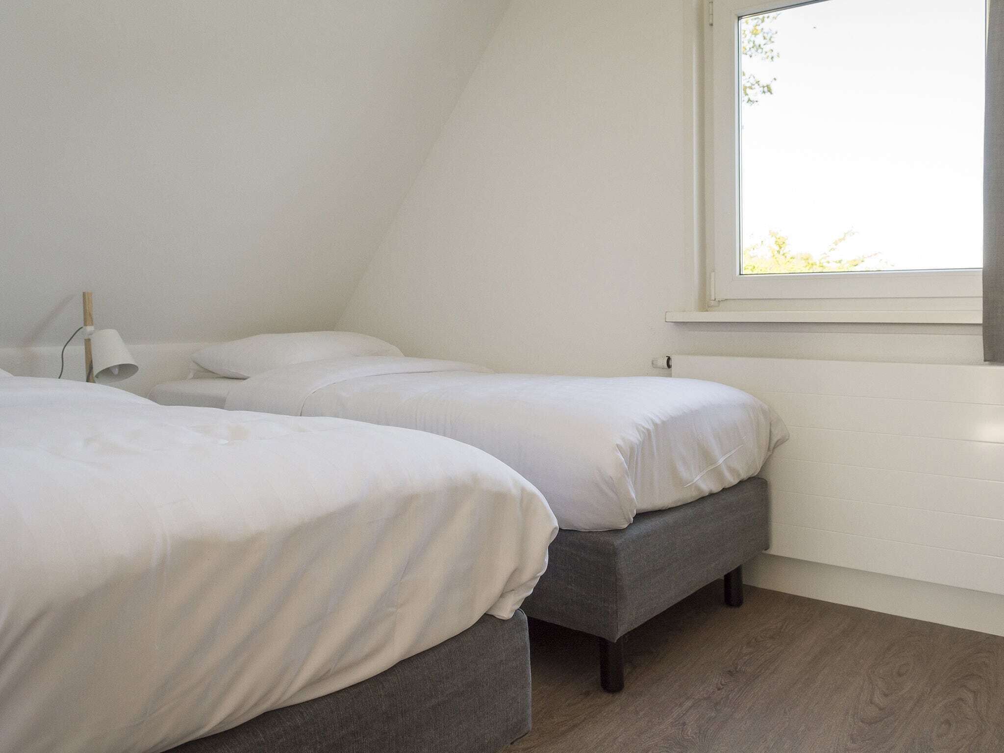 Une chambre avec deux lits, une fenêtre et une lampe.