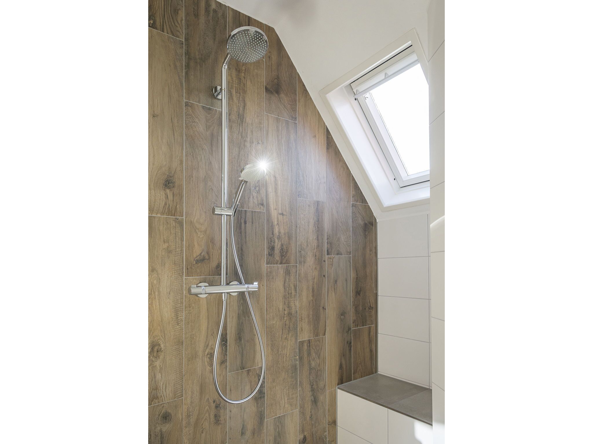 A shower with a rain shower head, a handheld showerhead, and a handheld shower hose.