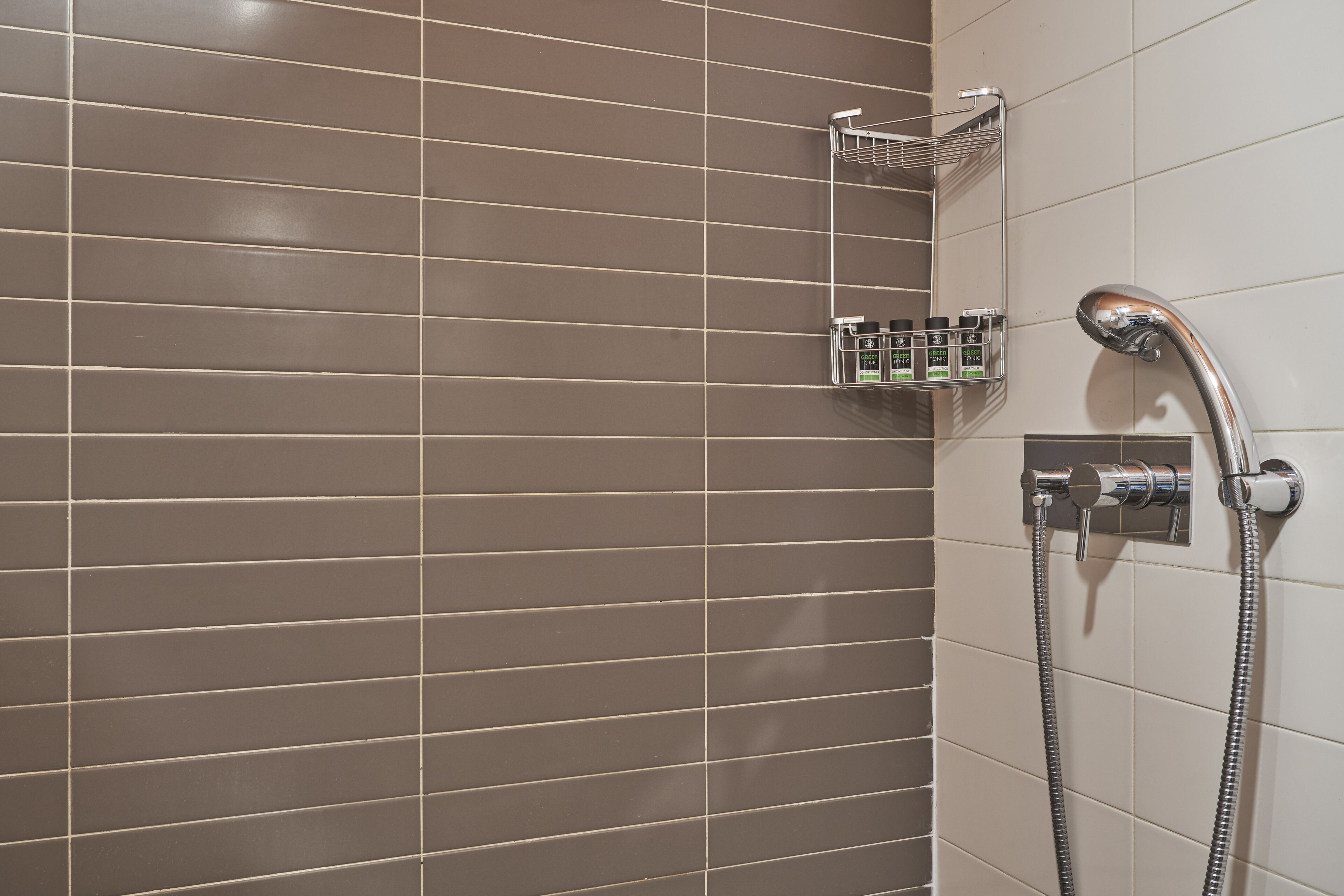 A bathroom with a shower area, a towel rack, and a soap dispenser.