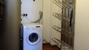Ein kleiner Hauswirtschaftsraum mit einer Waschmaschine mit Frontlader, einem großen Warmwasserbereiter und einem Wäscheständer aus Metall.