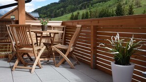 En træterrasse med et bord og stole, omgivet af et træhegn, med udsigt over et bjergrigt landskab.