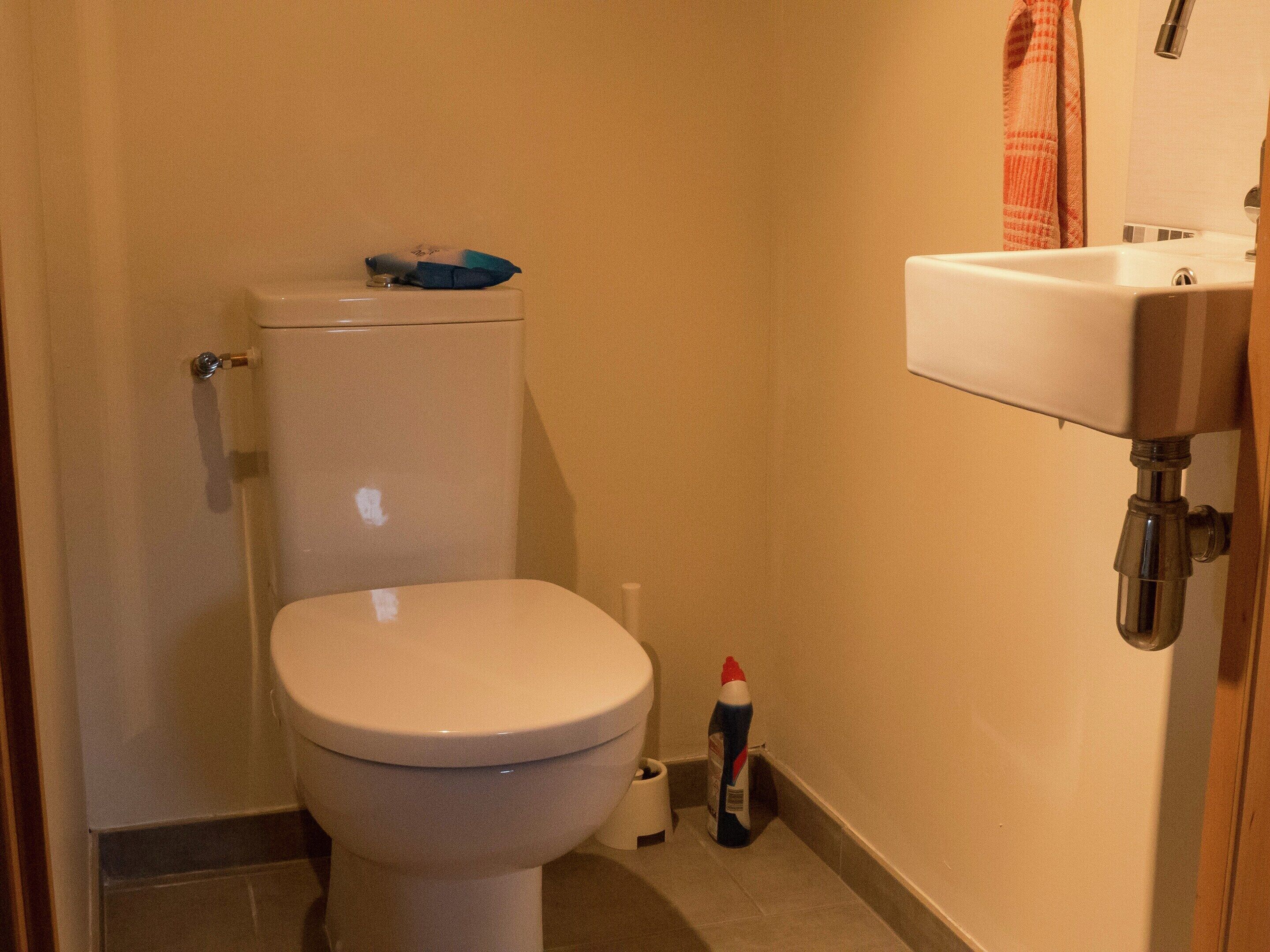 Ein kleines Badezimmer mit Toilette, Waschbecken und einer Reinigungsflasche.