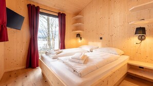 A wooden cabin bedroom with two beds, a TV mounted on the wall, and built-in shelves.