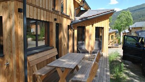 A wooden cabin with a deck, outdoor seating, and a car parked nearby.