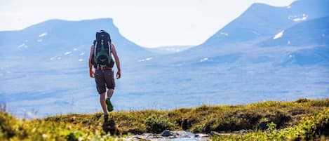 Una persona camina de excursión con una mochila sobre un terreno cubierto de hierba, con montañas al fondo.