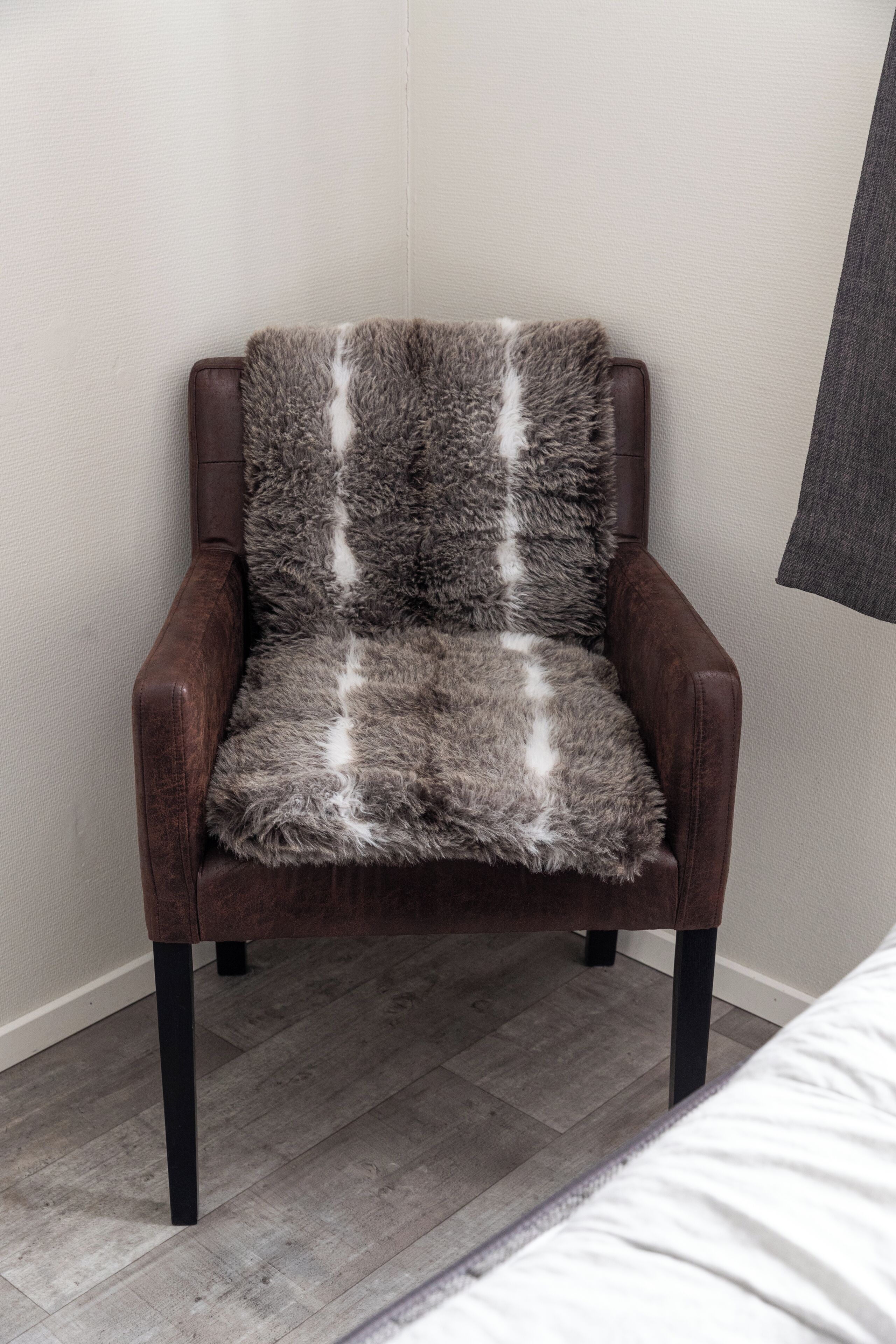 Una poltrona in pelle marrone con una soffice coperta grigio e bianca.