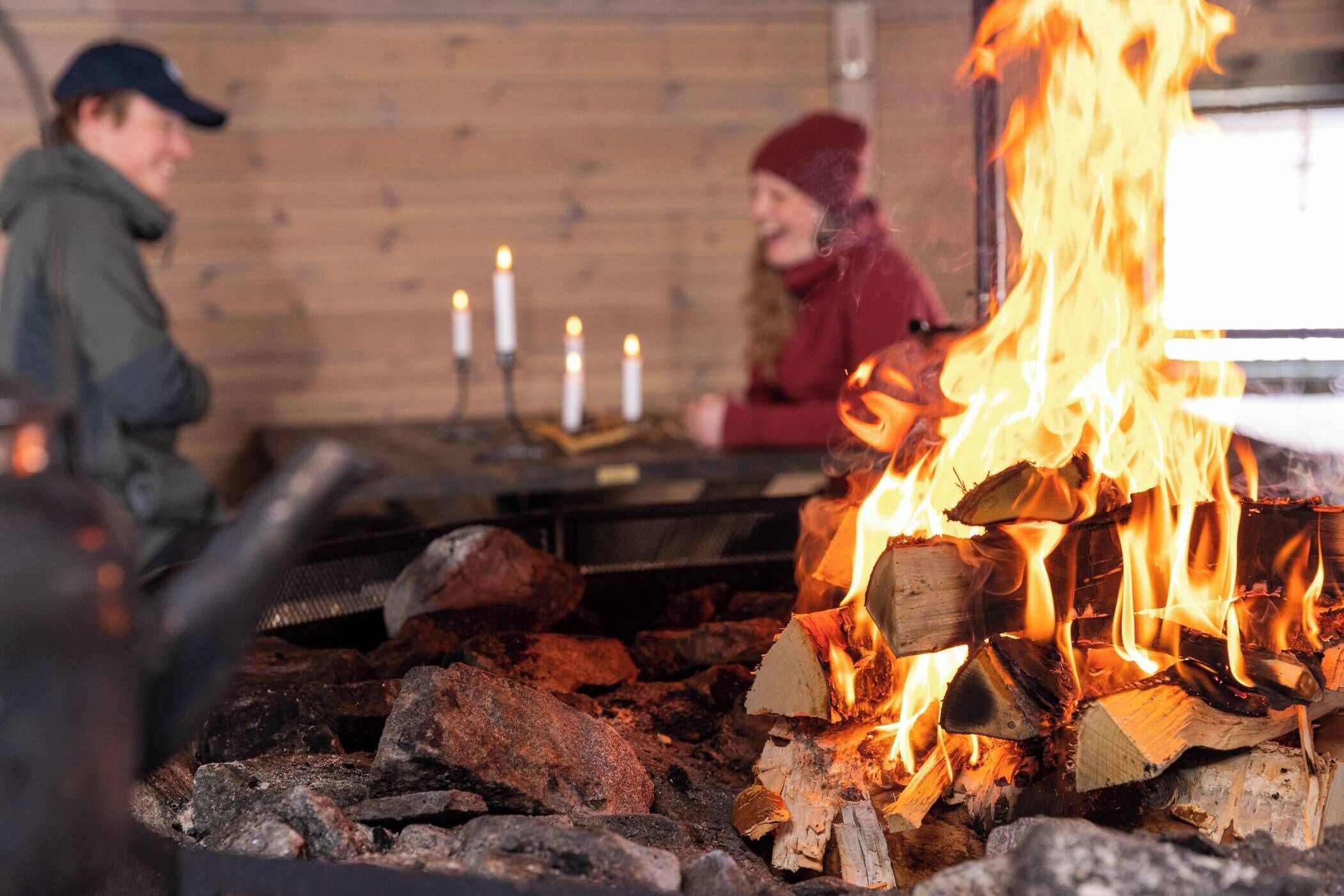 A cozy indoor setting with a fireplace, logs, and candles.