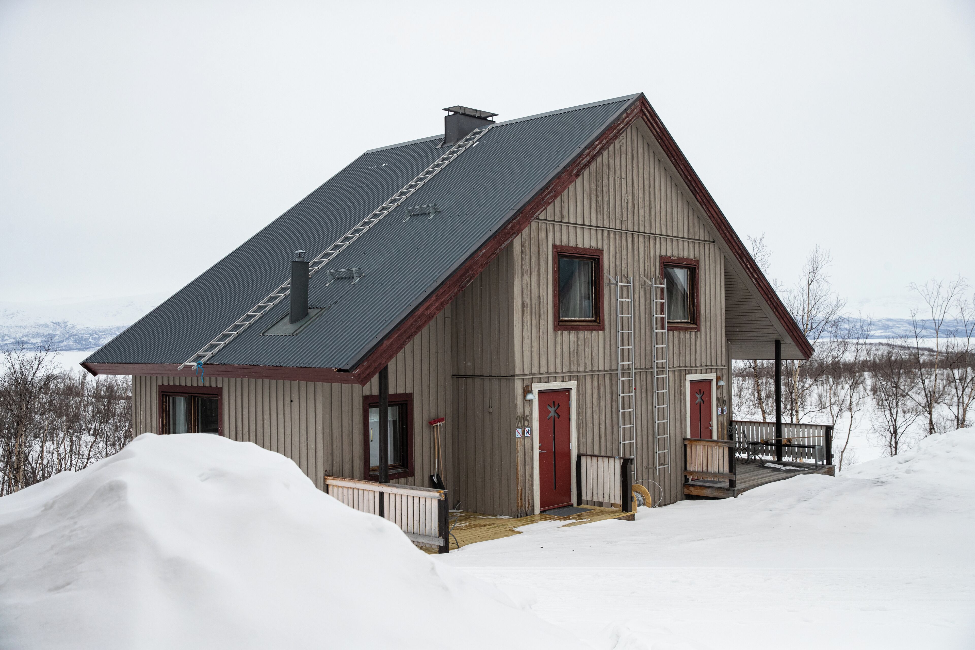 A wooden house with a sloped roof, a front porch, and a door with a red frame.