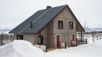 A wooden house with a sloped roof, a front porch, and a door with a red frame.