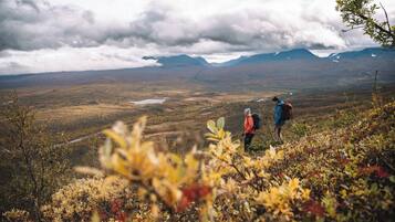 Um caminhante com jaqueta vermelha e calças azuis caminhando por uma trilha montanhosa carregando uma mochila.