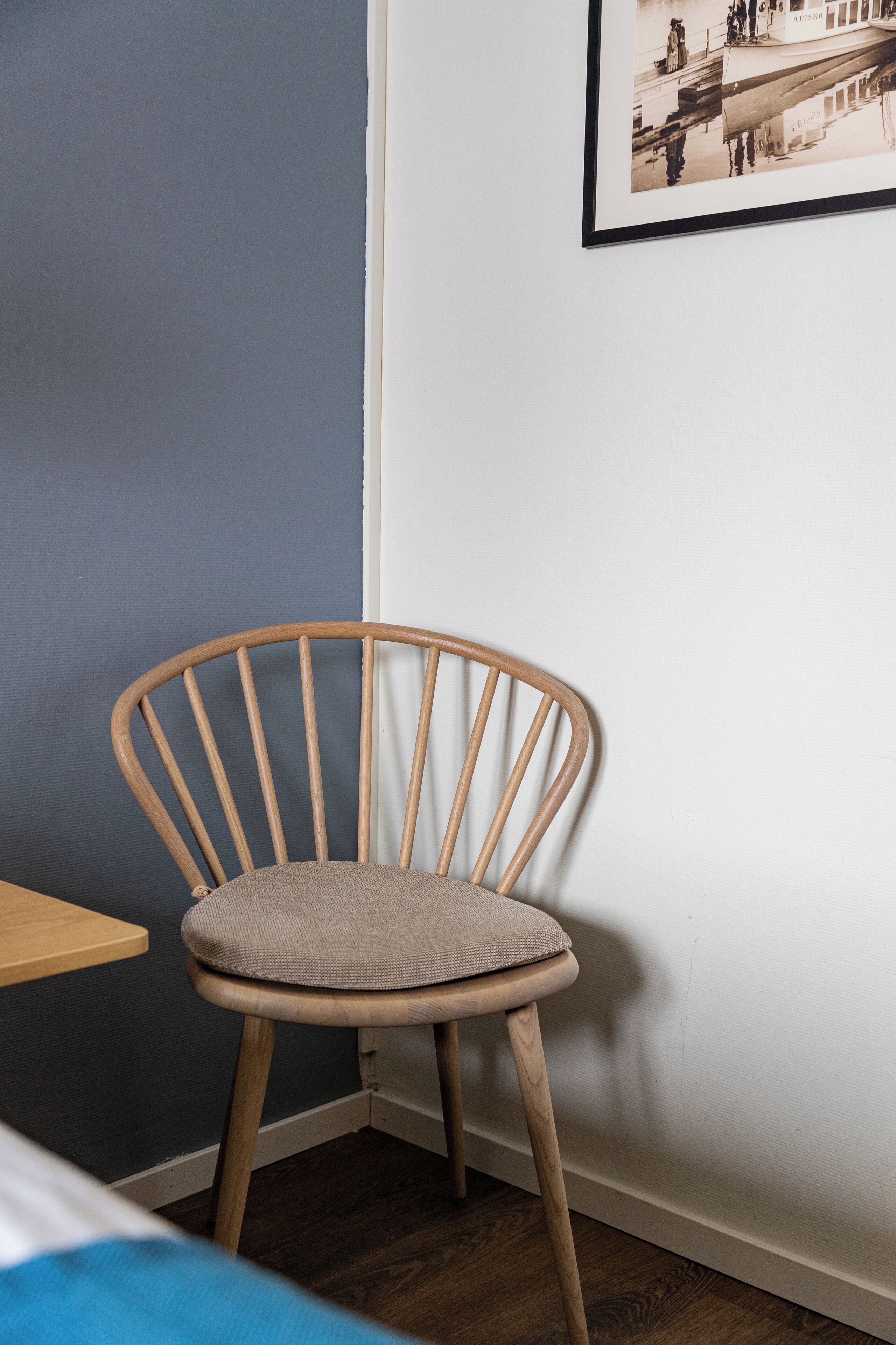 Eine Ecke eines Zimmers mit einem Holzstuhl, einem kleinen Tisch und einem gerahmten Bild an der Wand.