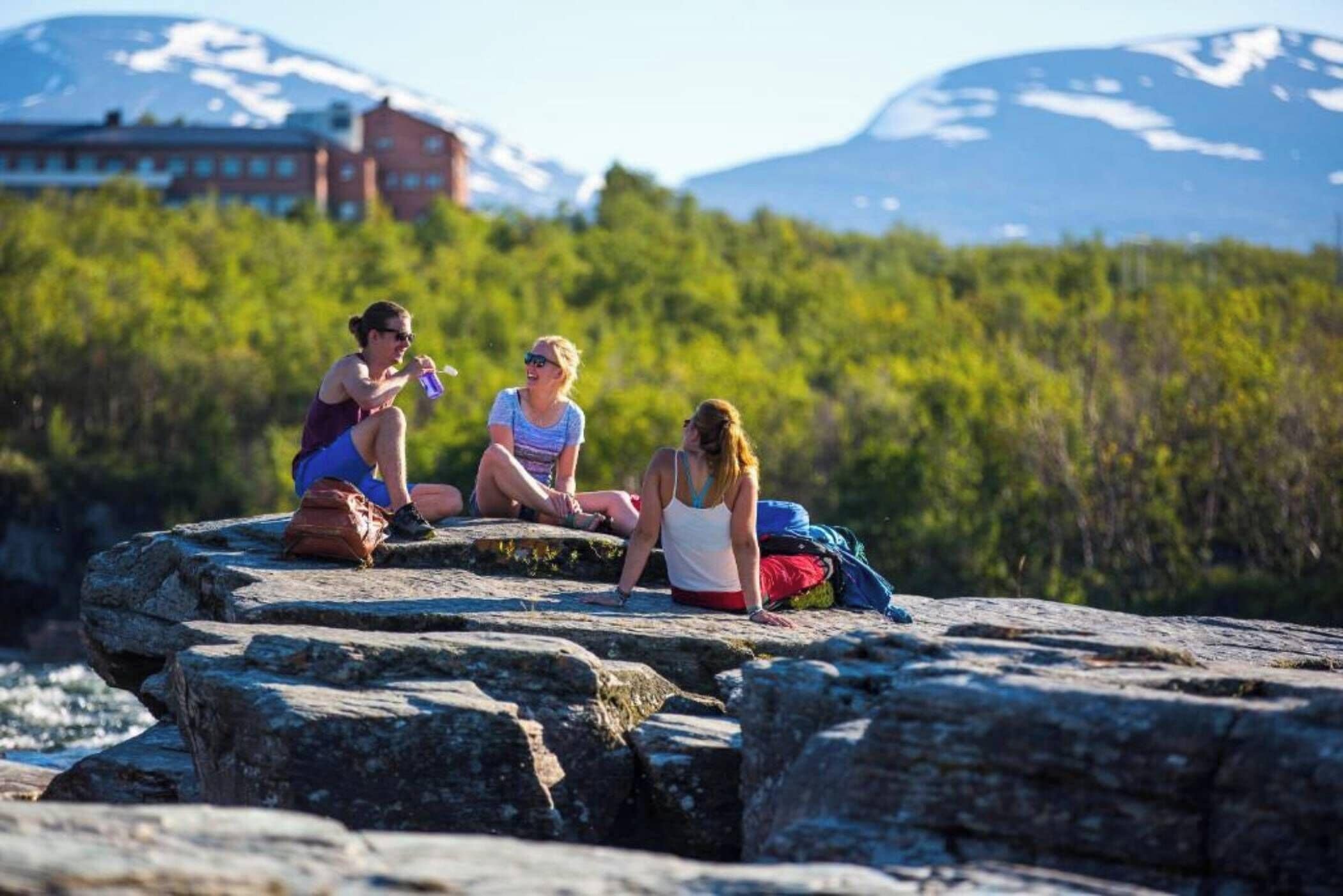 Trois personnes assises sur une formation rocheuse, avec une chaîne de montagnes en arrière-plan.