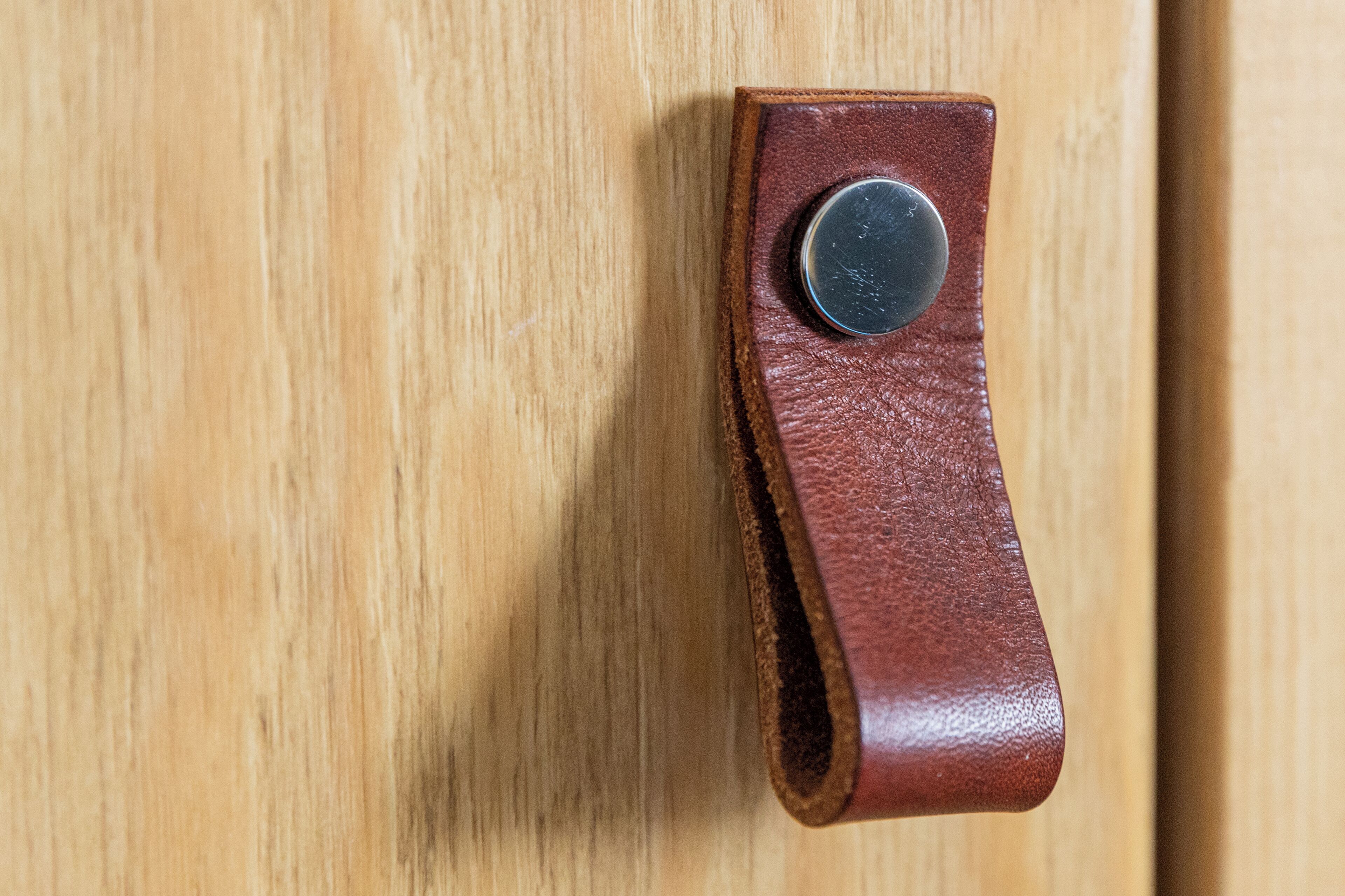 A brown leather strap with a round metal object attached to it, hanging on a wooden surface.