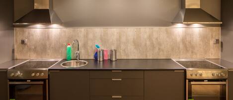 A modern kitchen with two ovens, a sink, and a stainless steel countertop.