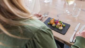 Una persona che cena a tavola, con un piatto di cibo, un bicchiere di vino e posate.