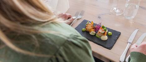 A person dining at a table with a plate of food, a wine glass, and cutlery.