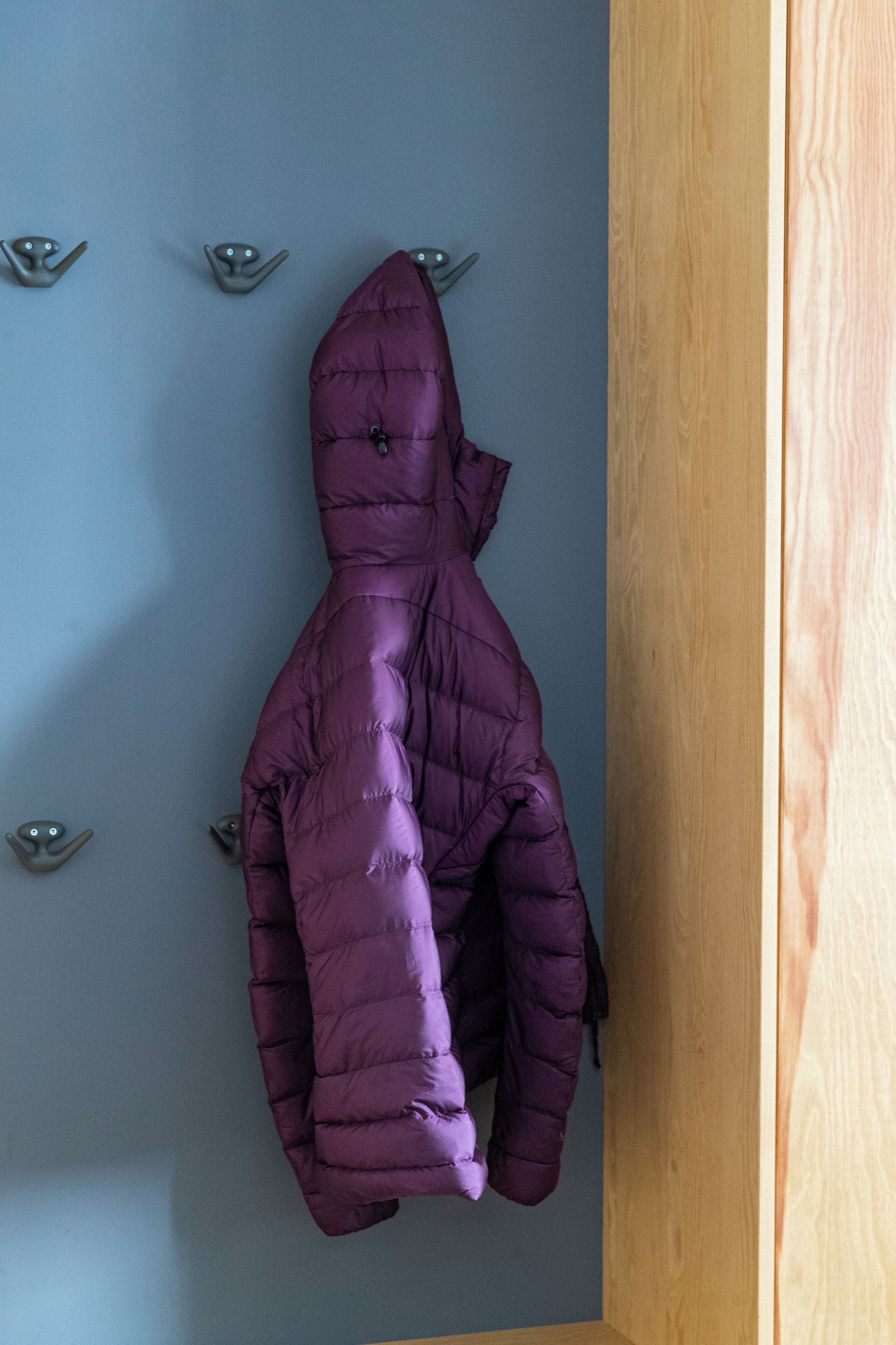 A purple puffer jacket hanging on a wall with hooks.