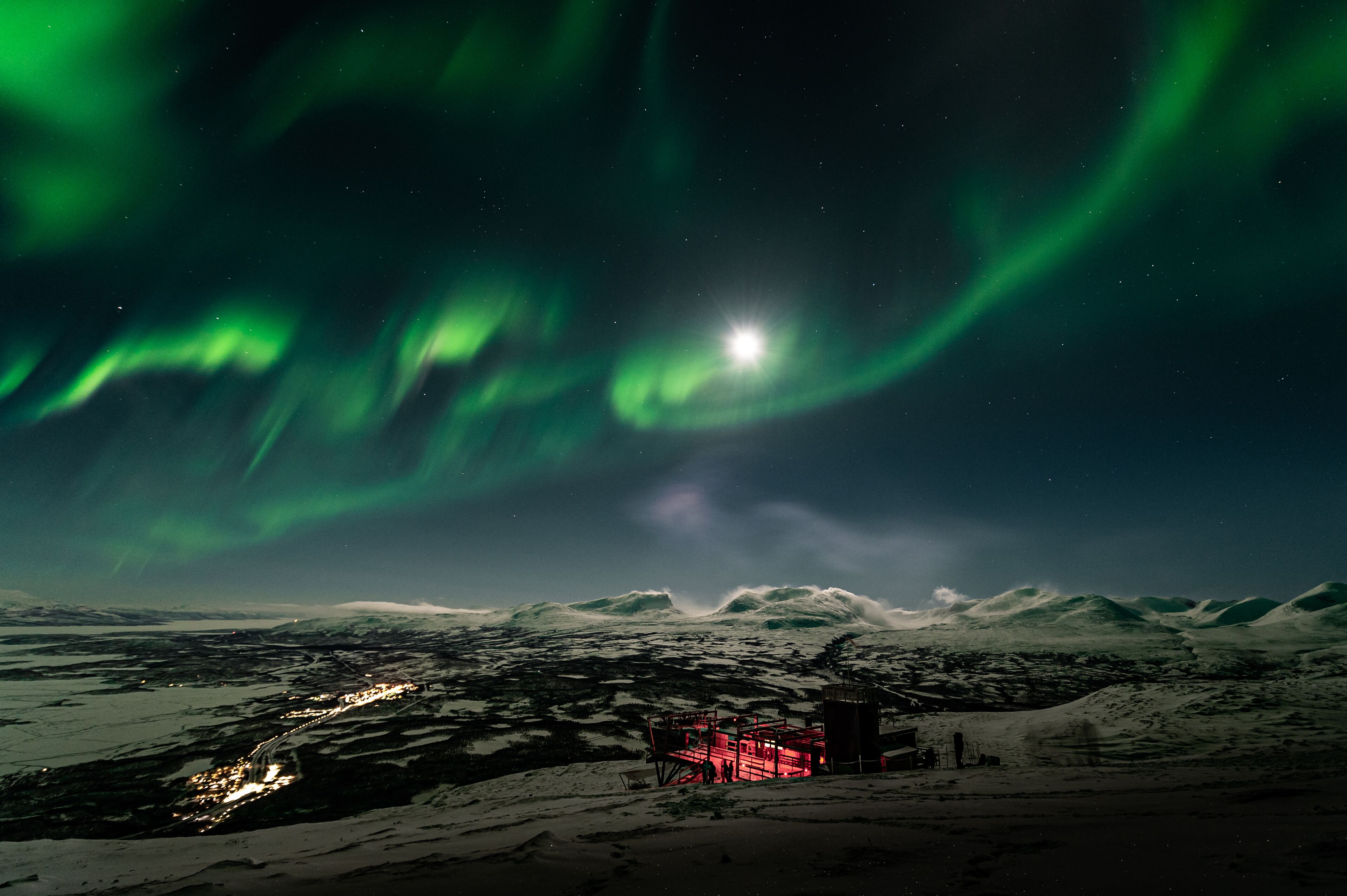 Un paysage enneigé avec un petit bâtiment et une structure illuminée de lumière rouge.