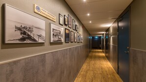 Un pasillo con piso de madera, una serie de cuadros enmarcados en la pared y un cartel sobre ellos.