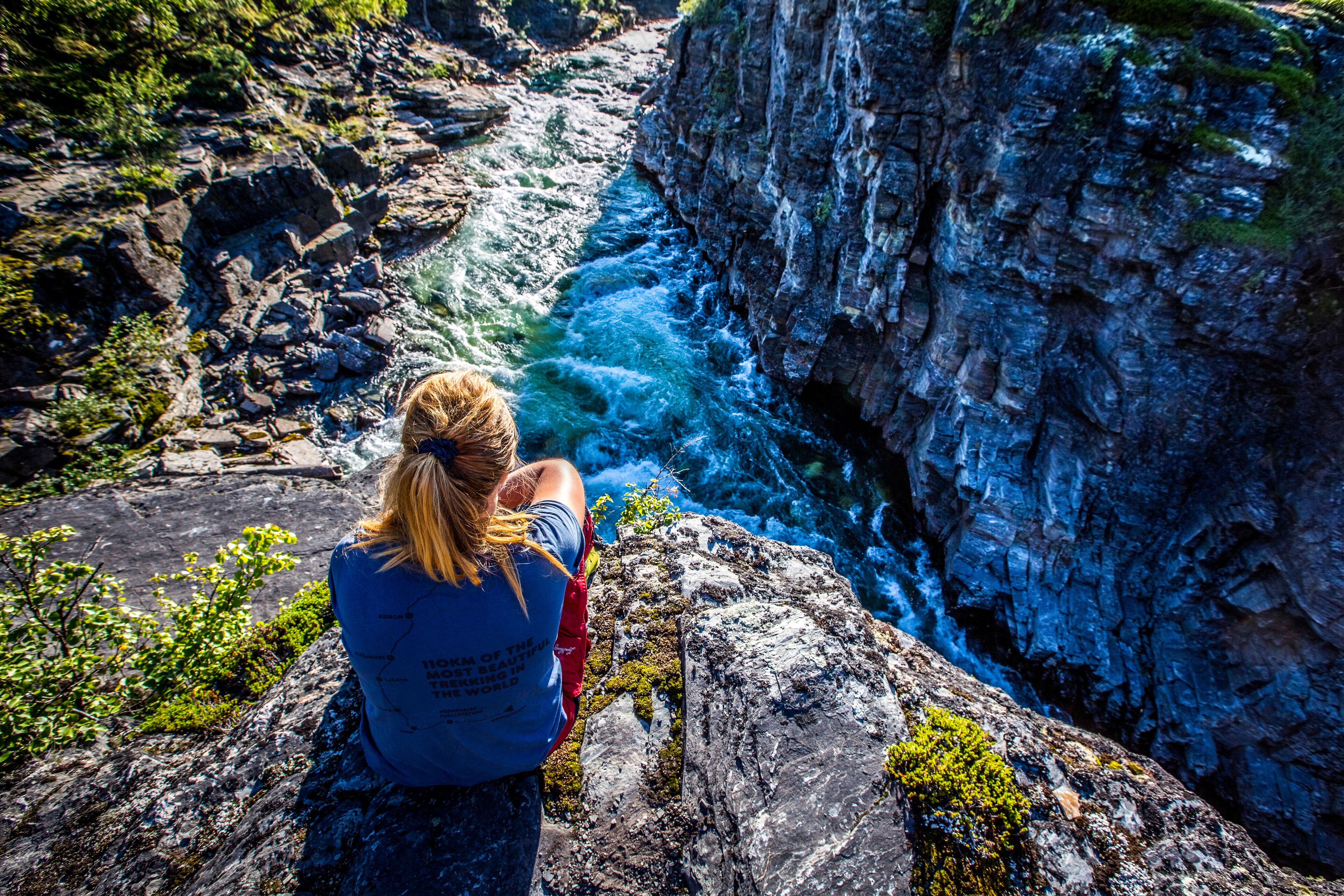 A person sitting on a rock overlooking a river with a rocky cliff.