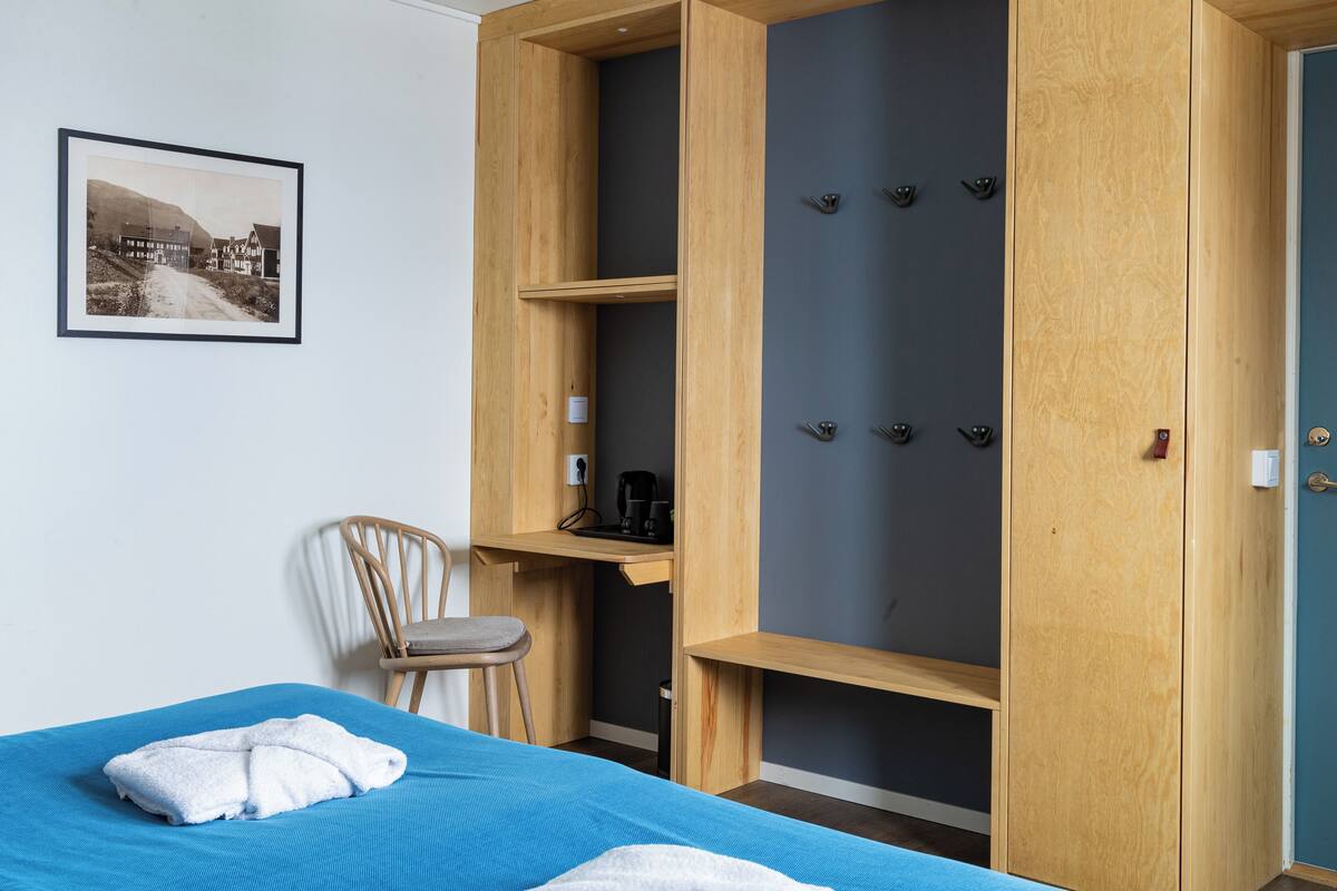A bedroom with a bed, a chair, a wooden wardrobe, and a framed picture on the wall.
